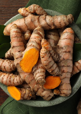 Fresh turmeric root in a bowl, one piece cut to show the orange interior